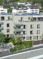 A modern apartment building with multiple floors, solar panels on the roof, balconies, and a garden area.