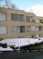 Apartment building with balcony, three floors, beige exterior, large windows, snowy surroundings
