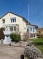 2 story house, yellow exterior, brown roof, garage, balcony, driveway, garden
