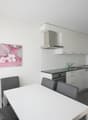 white tiled walls, kitchen with black countertop, white cabinets, modern appliances, grey chairs, dining table, artwork on wall, window with white curtains