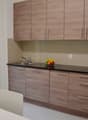 Modern kitchen with wooden cabinets, black countertop, stainless steel sink, and a dishwasher. Large windows provide natural light and a view of the exterior. The kitchen also includes a dining area with a table and chairs.