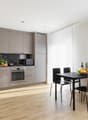 Modern kitchen with wood flooring, gray cabinets, oven, wooden dining table with chairs, bowl of fruit, bottle, glasses