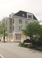 4-story apartment building with a modern design, gray exterior walls, and large windows. The building is surrounded by trees and landscaping, and there is a parking area in front of the building.