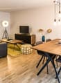 Open-concept living and dining area with hardwood floors, gray sofa, wooden dining table and chairs, TV stand, and decorative wall art