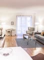 large windows, large gray couch, coffee table, glass table, armchair, desk, chair, two potted plants, wooden floor