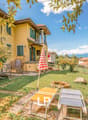 2 story house, yellow, green shutters, large backyard, deck, lounge chairs, trees, fence, mountains in the background