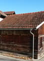 Raised ground floor, wooden walls, terracotta roof, mountains in the background, paved road