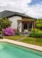 House with swimming pool, garden, patio with table and chairs, red and white exterior, mountain in the background