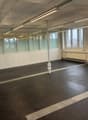 Empty room with white walls, black floor, glass partitions, windows, and overhead lighting.