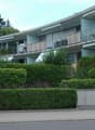 Two-story apartment building with balconies and awnings, surrounded by bushes and trees