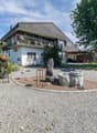 2 story house, gray roof, white walls, balcony, gravel driveway, garden, trees, outdoor seating