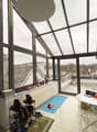 Room with large windows, a white table, a rug, and a shower head on the ceiling. The view outside the windows shows a snowy rooftop and cityscape.