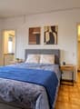 double bed, nightstands, bedside lamps, two paintings on the wall, sliding glass doors to the balcony, wooden floor