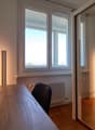 wooden desk, black chair, white candle, small potted plant, white radiator, large window, mirror door