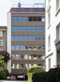 6 story building, glass windows, metal and wood exterior, cars parked at entrance, rooftop terrace