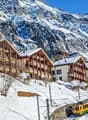 Wooden chalets, snow-covered mountains, yellow train on tracks, winter scenery