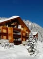 wooden chalet, multiple balconies, snow covered roof, surrounded by snow covered trees