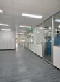 Empty office space with glass walls, white walls, gray floor, fluorescent ceiling lights, and a blue cabinet.