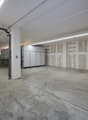 Empty room with concrete floor, white walls, unfinished ceiling, metal shelves, and metal pipes
