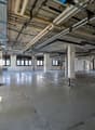 Empty room with concrete floor, metal beams, and visible pipes and wires on the ceiling