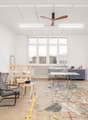 large room, white walls, ceiling fan, shelves with art supplies, tables, chairs, large windows, unfinished floor