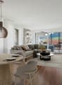modern living room with a couch, dining table, and chairs, wooden floor, large windows, balcony, and a view