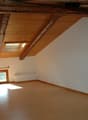 Empty room with wooden floor, wooden ceiling, two windows, and white walls.