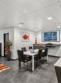 Open-concept living and dining area with modern, minimalist decor. The space features a large TV and entertainment system, a dining table with chairs, and a kitchen area with a dishwasher. The walls are decorated with colorful artwork, and the room has a
