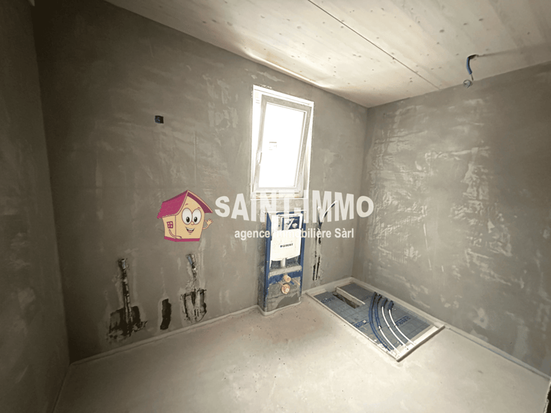 Unfinished room with gray walls, a window, and construction materials such as a ladder and pipes visible.