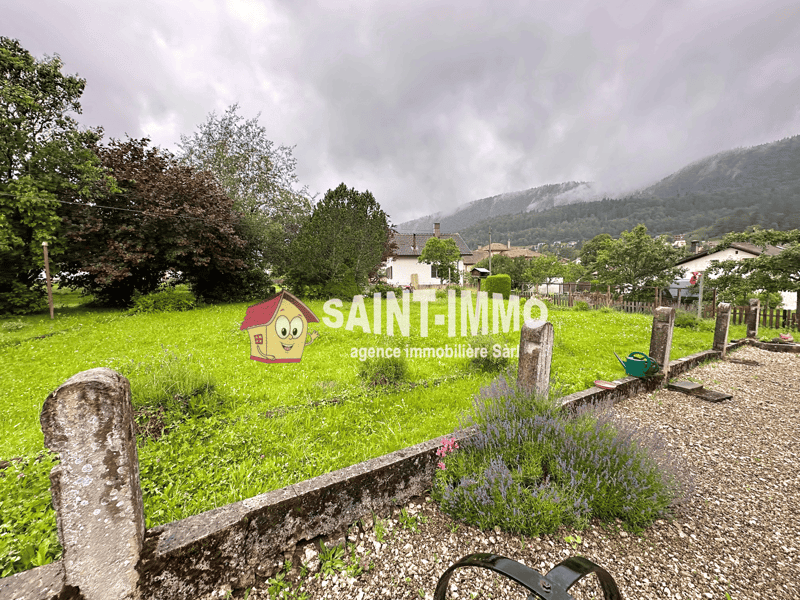 Plot of land, green grass, small bushes, gravel path, mountains in the background