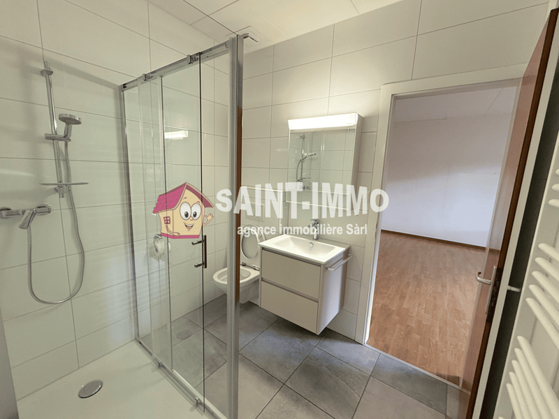 Glass walk-in shower, white tile flooring, white vanity with sink, toilet, wooden floor in adjacent room, open door leading to another room, white walls