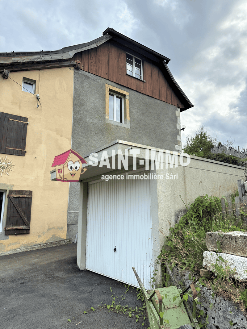 Two-story house with a tiled roof, grey exterior wall with wooden elements, windows with wooden shutters, white garage door, driveway