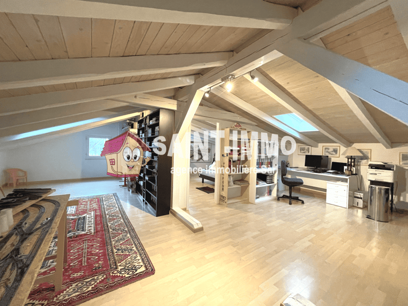 Spacious attic conversion with wooden beams and skylights, hardwood flooring, shelving unit, desk and office setup, and a decorative rug