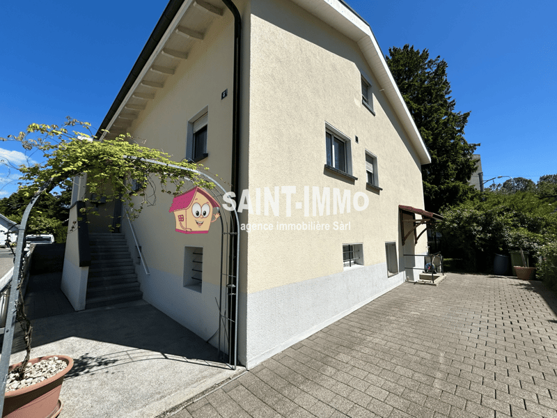 2-story house, beige walls, white windows, black door, paved driveway, staircase, front balcony, potted plants