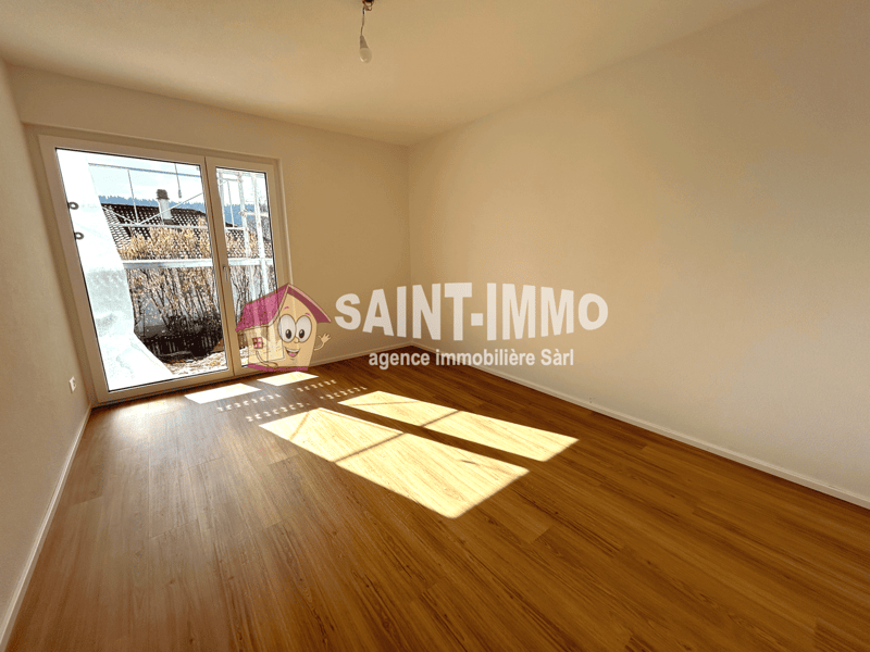 Empty room with hardwood flooring, white walls, and a large window. The room has a Saint-Immo real estate agency logo painted on the wall.