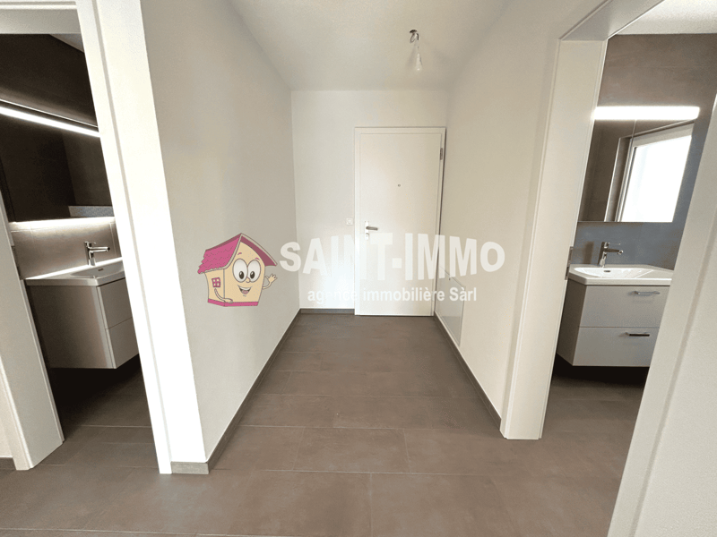 The image shows the interior of an apartment. The entrance hallway has a white door and walls, with a tiled floor. There is a logo for a real estate company, 'Saint-Immo', visible on the wall. The hallway leads to other rooms, including what appears to be