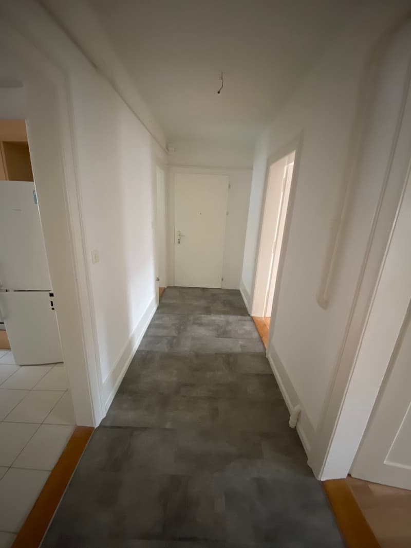 An empty hallway with grey tiles and white walls.