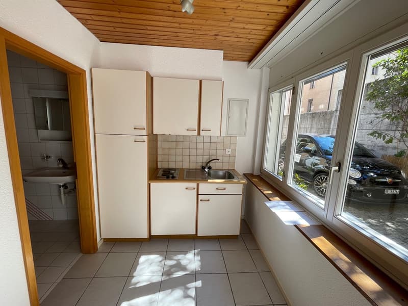 small kitchen with sink, stove, and cabinets, large window with view of a car