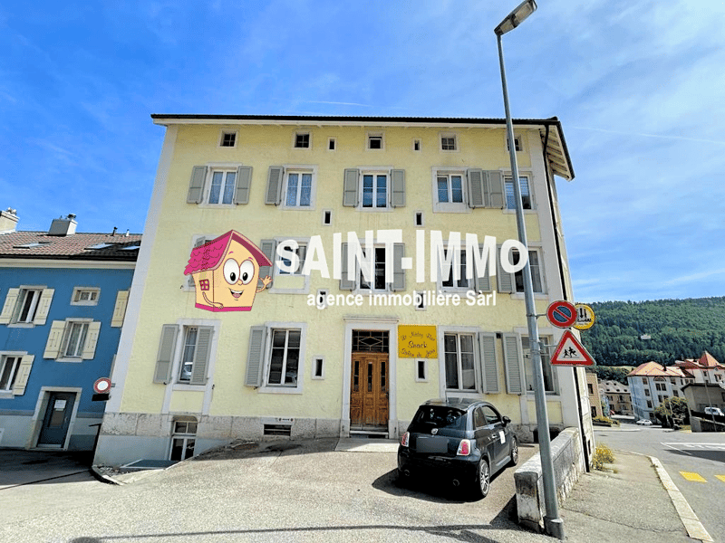 A yellow building with multiple windows and a sign reading 'SAINT-IMMO'. A black car is parked in front of the building.