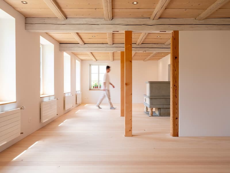 Fireplace on one wall, wooden floors, wooden columns, tall windows, white walls, three radiators on the left
