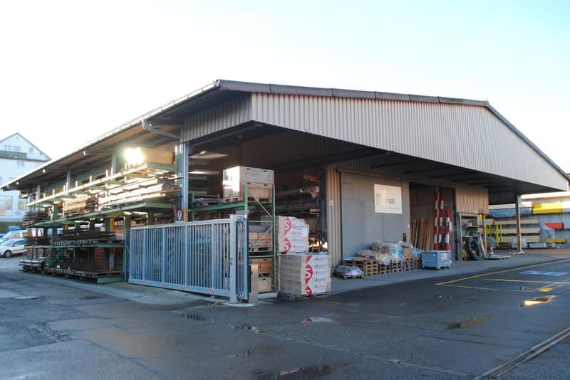 Warehouse building with large metal gate and shelving for storage, outdoor lighting, and an open yard