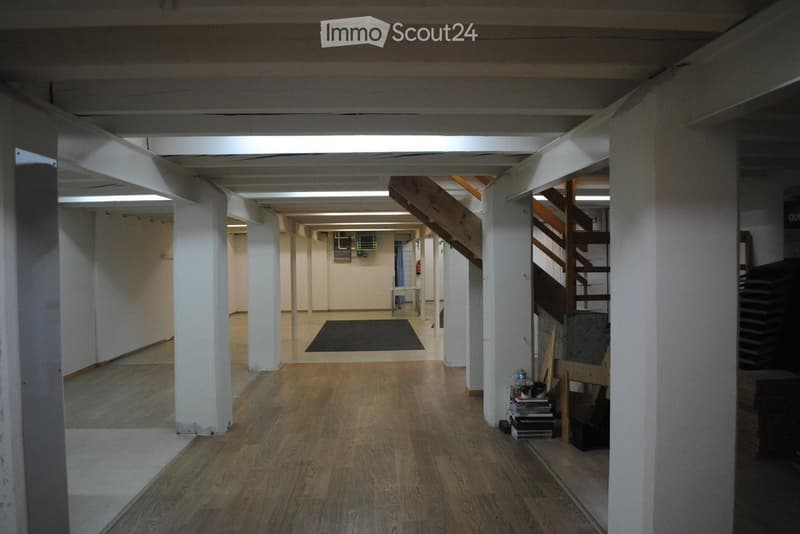 long hallway, hardwood flooring, white pillars, wooden staircase, black rug