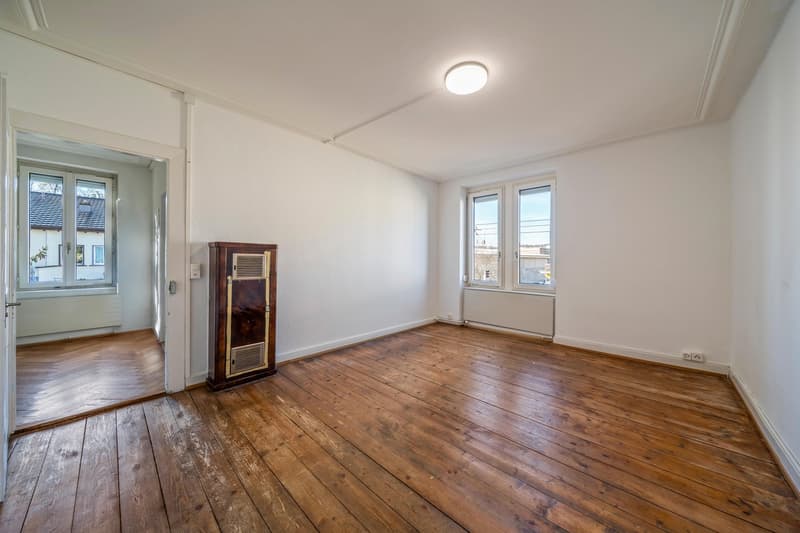 empty room, wooden flooring, two windows, wooden cabinet with radiator