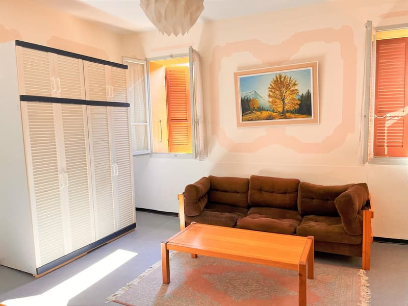 A room with a large white cabinet with sliding doors, a couch, a coffee table, a rug, and two windows with shutters