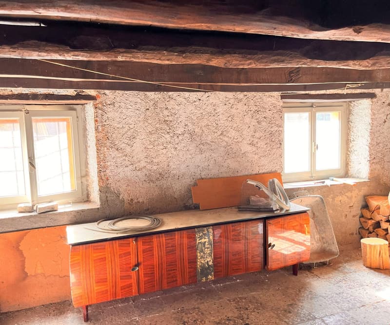 Old stone wall, wooden cabinet, two small windows, pile of wood, wooden beams
