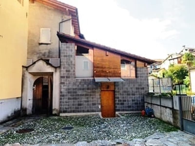 A two-story stone building with a large wooden door, brick wall, and gravel ground.