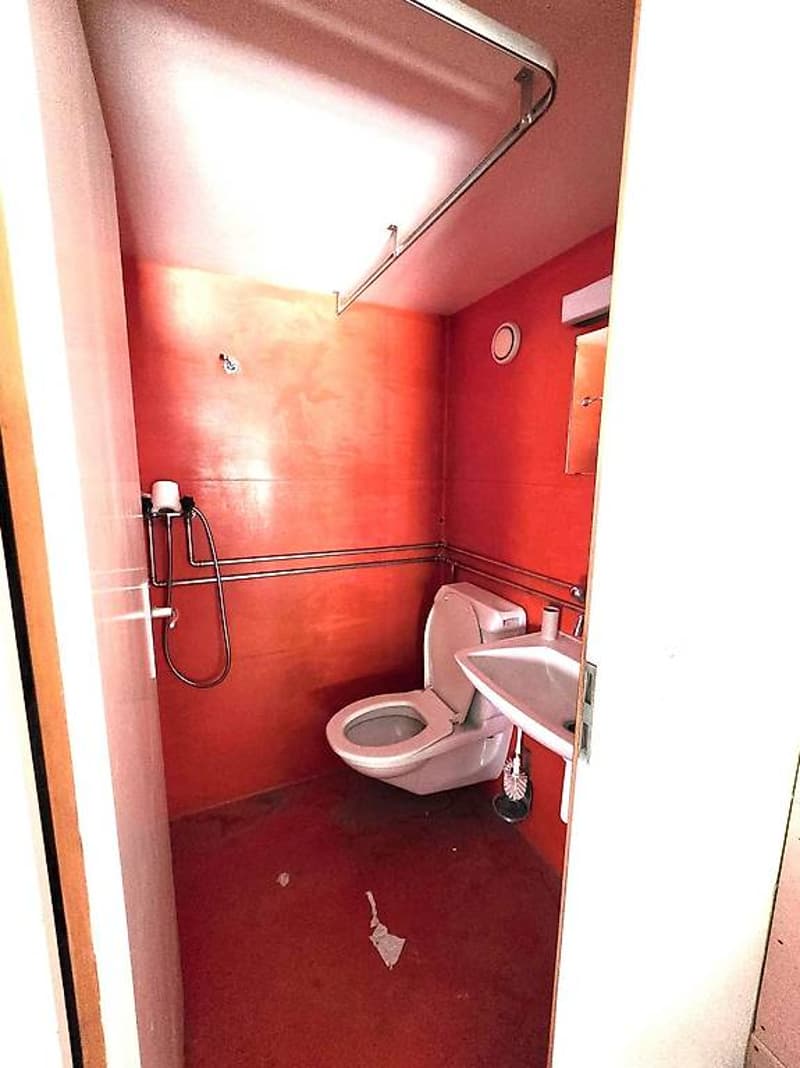Small bathroom with red tiles, white toilet, sink, showerhead