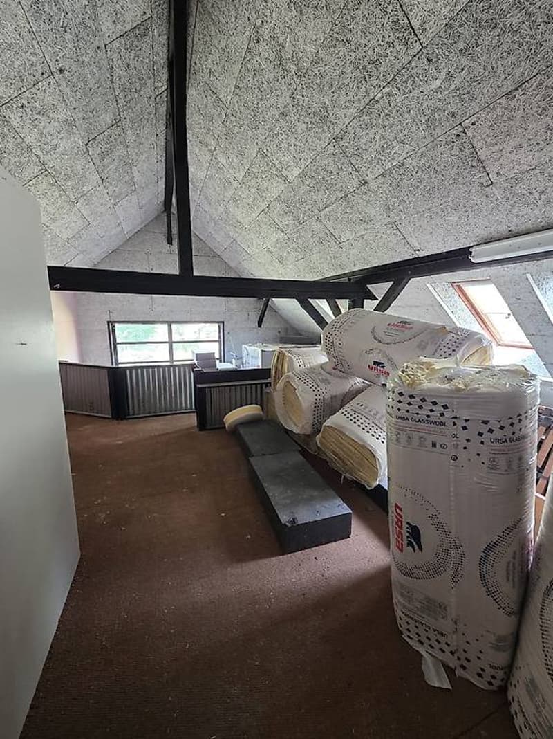 unfurnished attic room, white wall, brown floor, metal truss, rolled-up insulation materials, windows