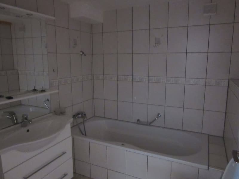 Bathroom with white tiles, bathtub, sink, mirror, and cabinet
