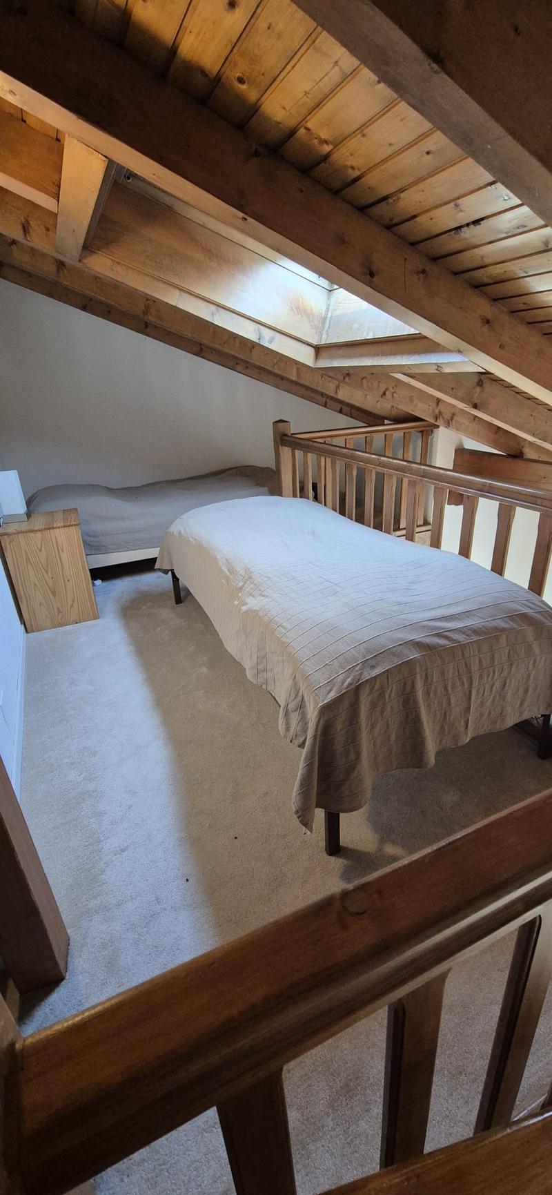 Carpeted floor, wooden ceiling beams, small size bed, wooden railings